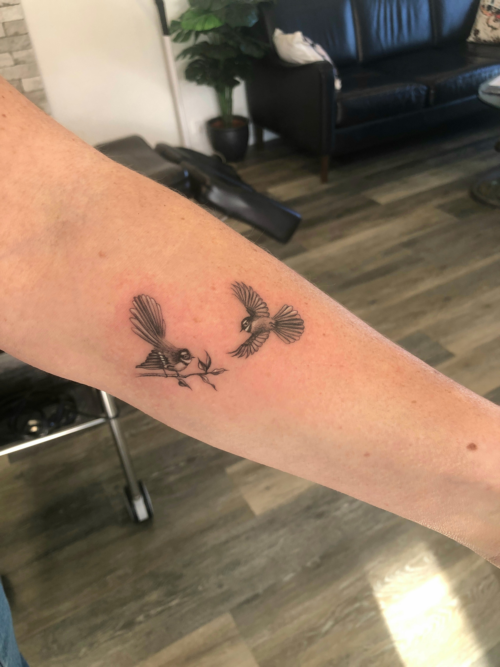 Black and grey tattoo of two miniature fantails, one perched on a branch and one in flight.